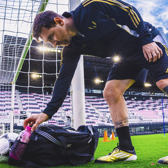 Messi grabbing a bottle of Más by Messi from a bag on the field.