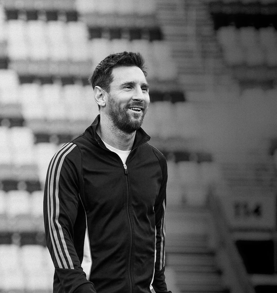 Leo Messi, founder of Más+ by Messi, stands in front of a blurred, empty stadium in the background.