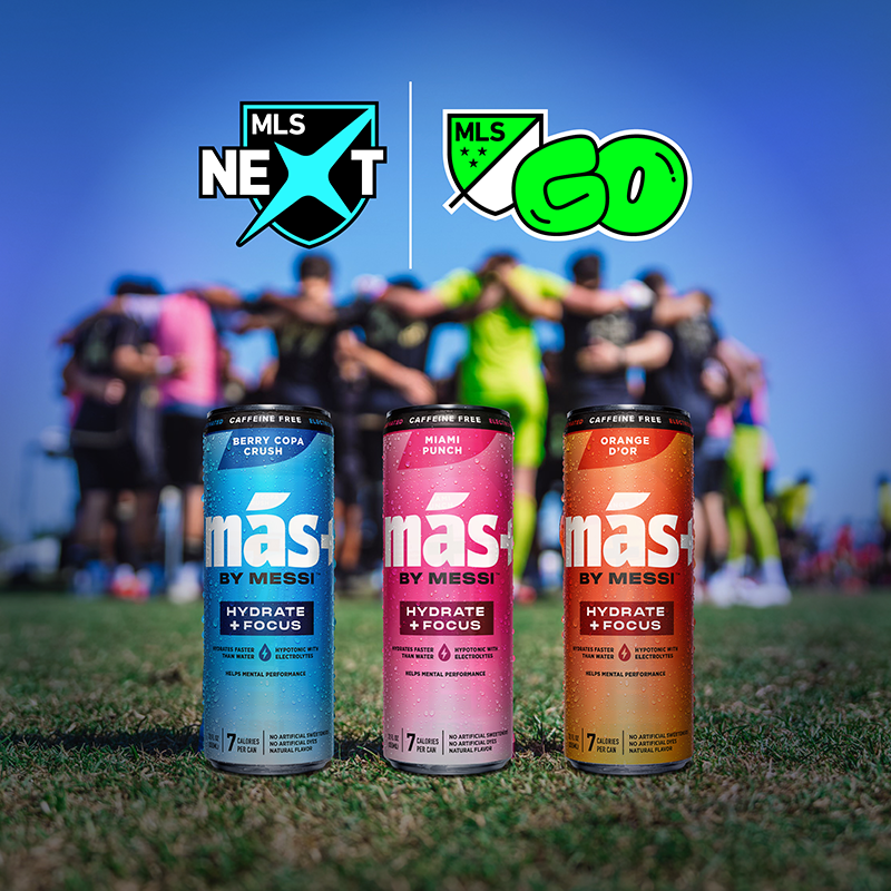 Three cans of Más+ by Messi drink on a soccer field, with blurred players and MLS NEXT and MLS GO logos visible.