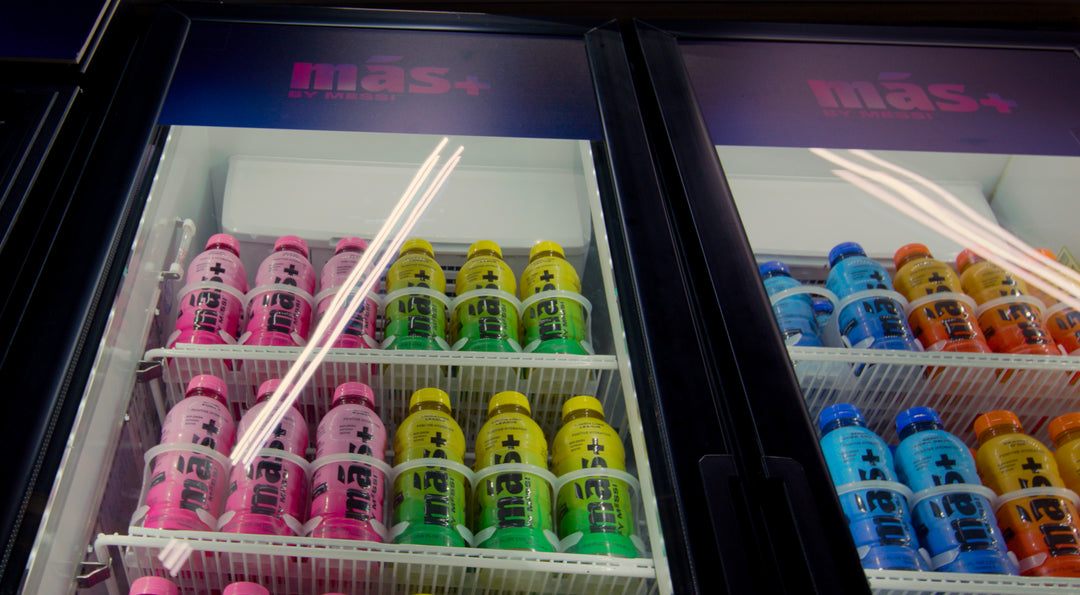 A refrigerator filled with several bottles of Más+ by Messi drinks in various colors and flavors.