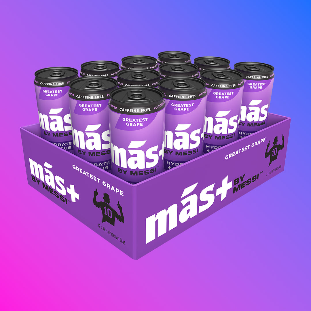 A purple cardboard tray holding twelve cans of Más by Messi Greatest Grape flavored, caffeine-free drink.